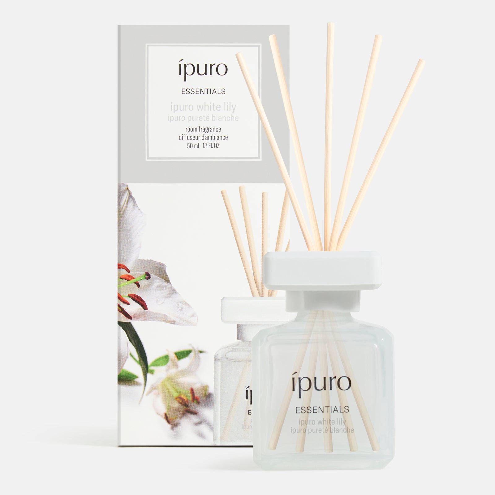 Ein klarer Glasflakon mit der Aufschrift ipuro Raumduft white lily with wooden reeds steht vor seiner Schachtel, die die Marke ipuro trägt und einen zarten, blumigen Duft nach weißen Lilien verspricht.