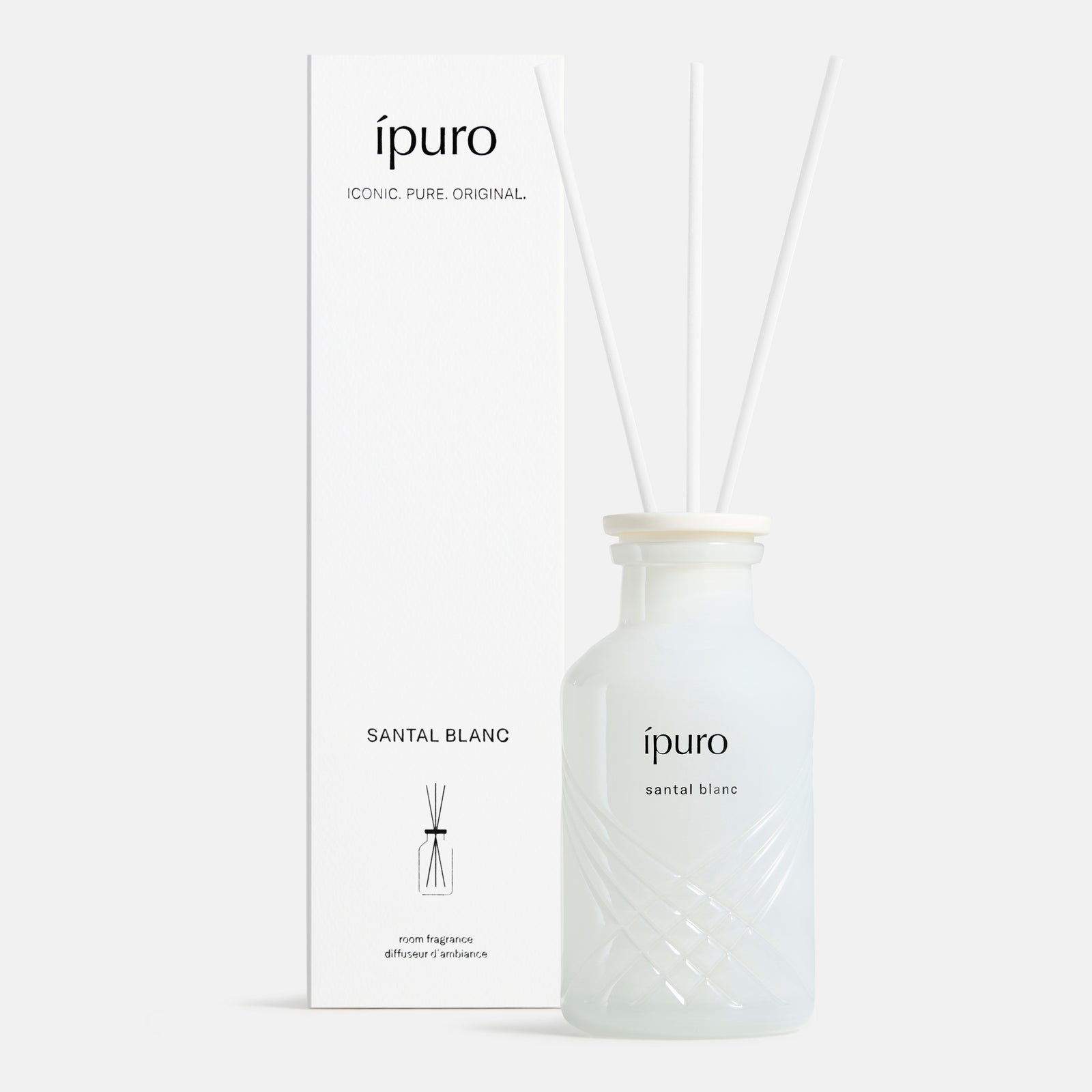 Ein weißer ipuro santal blanc Raumduft-Glasflakon mit drei weißen Diffusorblättern steht neben einer passenden hohen Schachtel mit schwarzem Text und minimalistischem Design, die den Duft von Sandelholz und zarter weißer Orchidee verströmt.