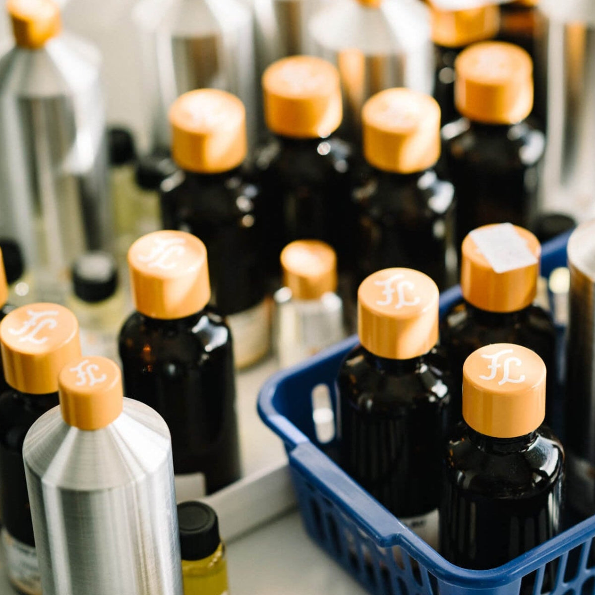 Mehrere braune Glasflaschen mit orangefarbenen Verschlüssen, einige mit weißem Logo, sind zusammen mit einigen Metall- und Kunststoffbehältern gruppiert. Die Flaschen sind in weißen und blauen Plastikschalen auf einer Fläche aufgestellt.