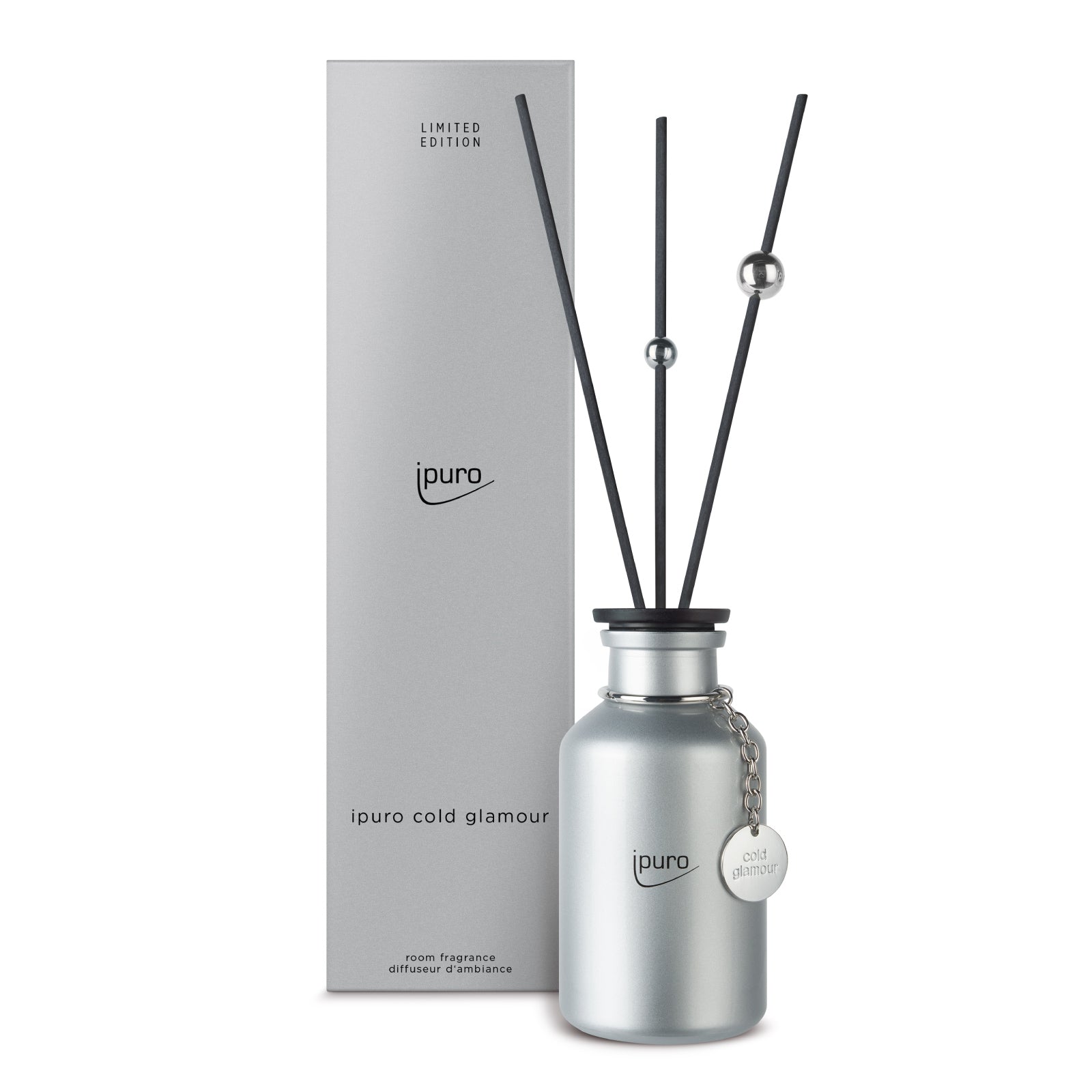 Eine silberne Flasche ipuro cold glamour Raumduft 240ml mit schwarzem Schilfrohr und einem runden Anhänger steht neben der passenden silbernen ipuro Limited Edition Box.