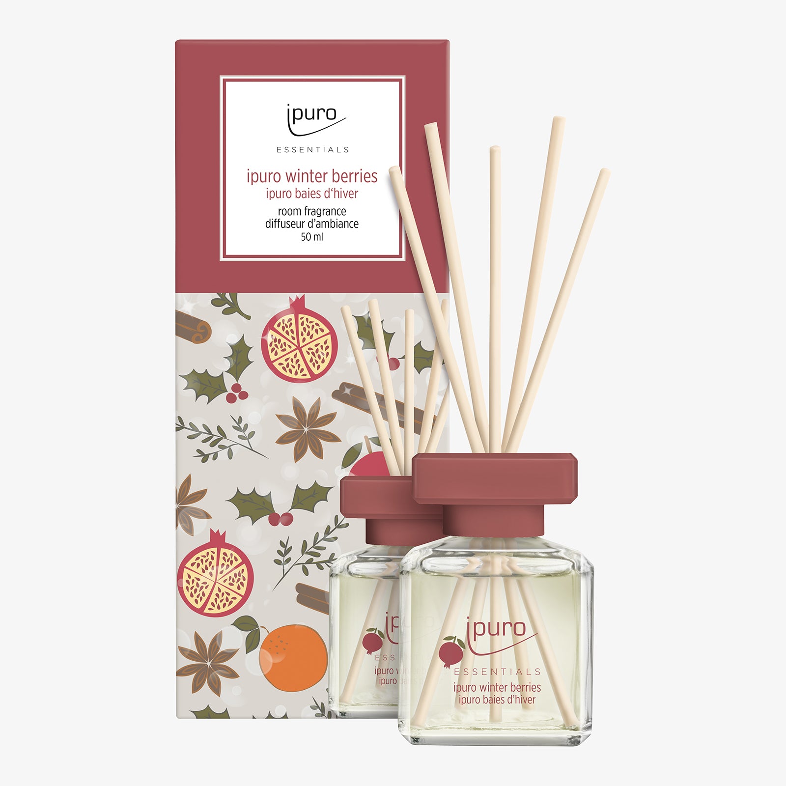 Ein 50 ml ipuro ESSENTIALS Raumduft Winter Berries mit Holzstäbchen wird neben seiner mit Beeren, Orange und Sternanis illustrierten Schachtel präsentiert. Der Duft enthält Noten von Beerennoten und Gewürznelke.